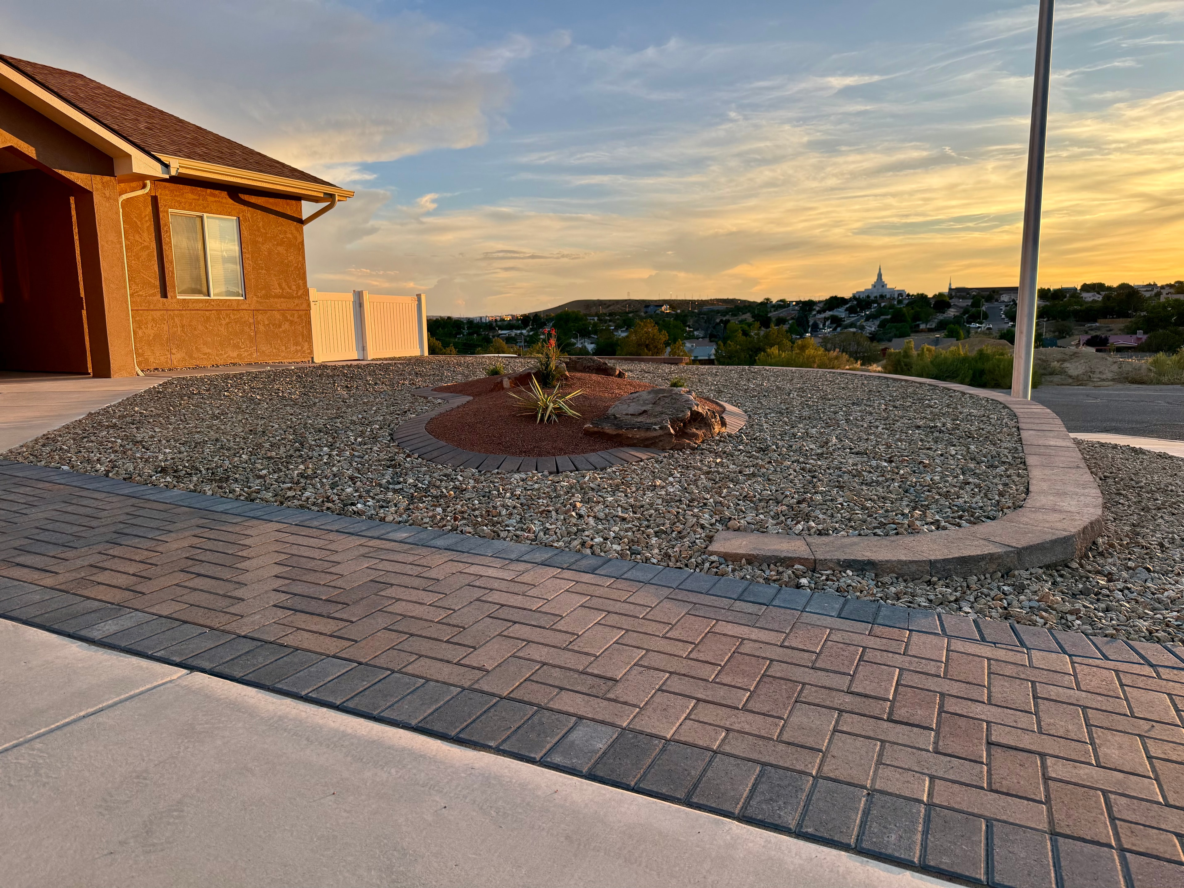 Paver driveway extension with raised planting bed, moss rock, paver border edging, and decorative gravel in Farmington NM — High Desert NativeScapes