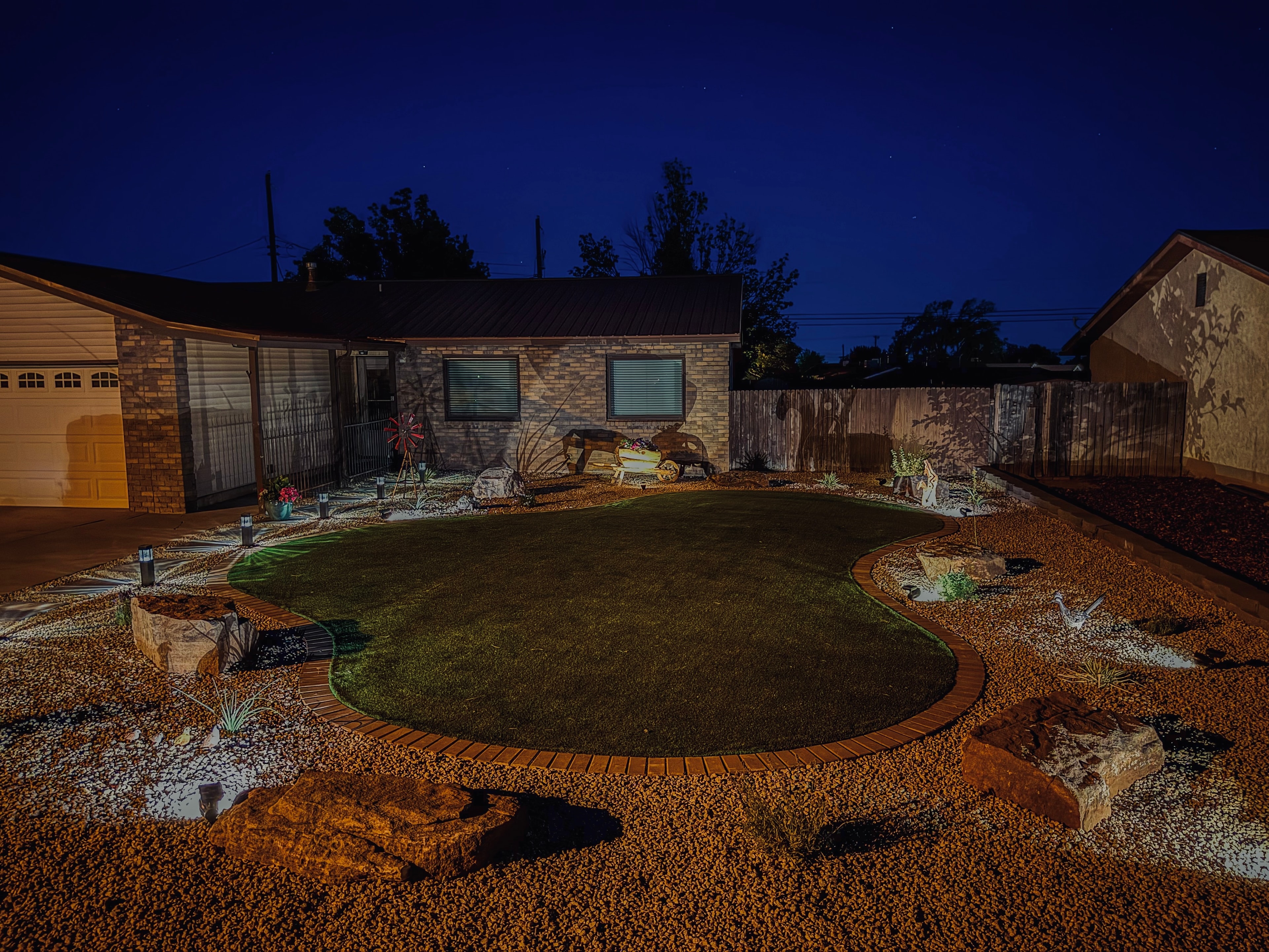 Artificial turf front yard with paver border, moss rock, decorative gravel, and landscape lighting at night in Farmington NM — High Desert NativeScapes